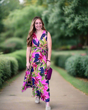Woman in a colorful floral dress standing against a gray wall.