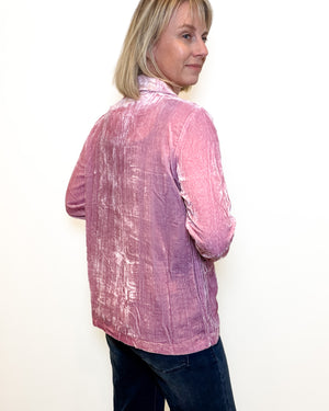 A woman wearing a textured, crinkled pink long-sleeve shirt and dark blue jeans, shown from a side-back angle against a plain white background.