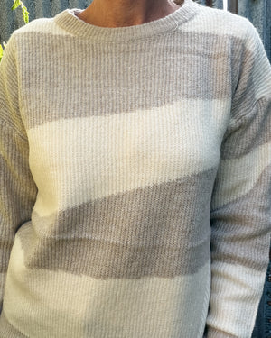 A close-up of a person wearing a ribbed knit sweater with wide horizontal stripes in cream, light taupe, and off-white.