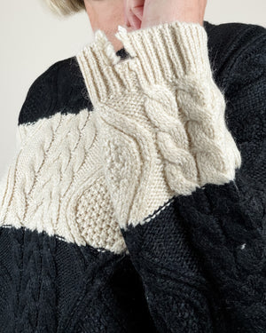 Close-up of a person wearing a chunky cable-knit sweater with a color-block design in black and cream.