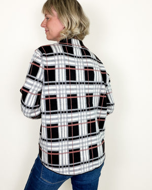 A woman wearing a black, white, and gray plaid flannel shirt with thin red accent lines, shown from a side-back angle against a plain off-white background.