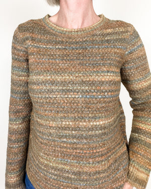 A close-up of a person wearing a long-sleeve knit sweater with horizontal marled stripes in earthy tones of brown, beige, muted blue, and olive green.