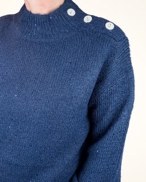 Close-up of a navy blue knit sweater worn by a model, featuring three silver rhinestone-embellished shoulder buttons and subtle sparkly flecks throughout the fabric.