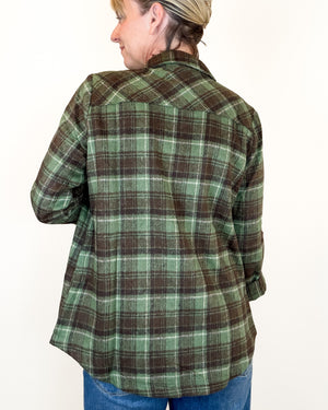 A woman shown from the back wearing a green and brown plaid flannel shirt with blue jeans, against a plain white background.