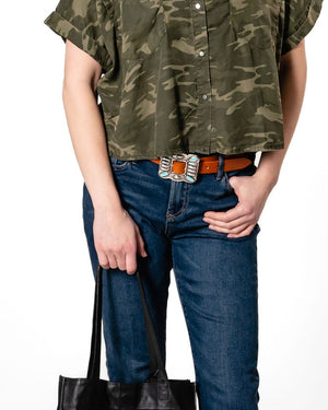 Woman wearing a green camouflage shirt and blue jeans, holding a black tote bag on a white background