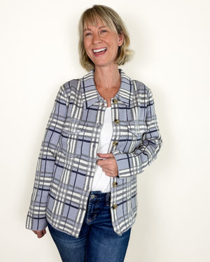 A woman modeling a gray and white plaid button-up jacket over a white top and blue jeans, standing against a plain off-white background.