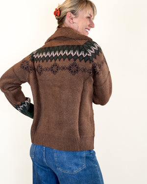A woman wearing a brown knit sweater with a dark green and pink Fair Isle yoke pattern, shown from the back against a plain off-white background.