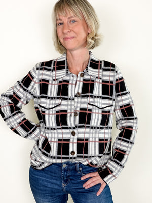 A woman wearing a black, white, and gray plaid button-up shirt with thin red accent lines, paired with blue jeans, standing against a plain off-white background.