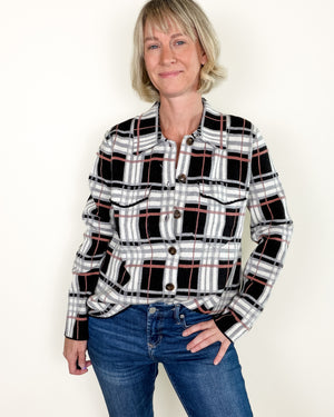 A woman modeling a black, white, and gray plaid button-up shirt with thin red accent lines, paired with blue jeans, against a plain off-white background.