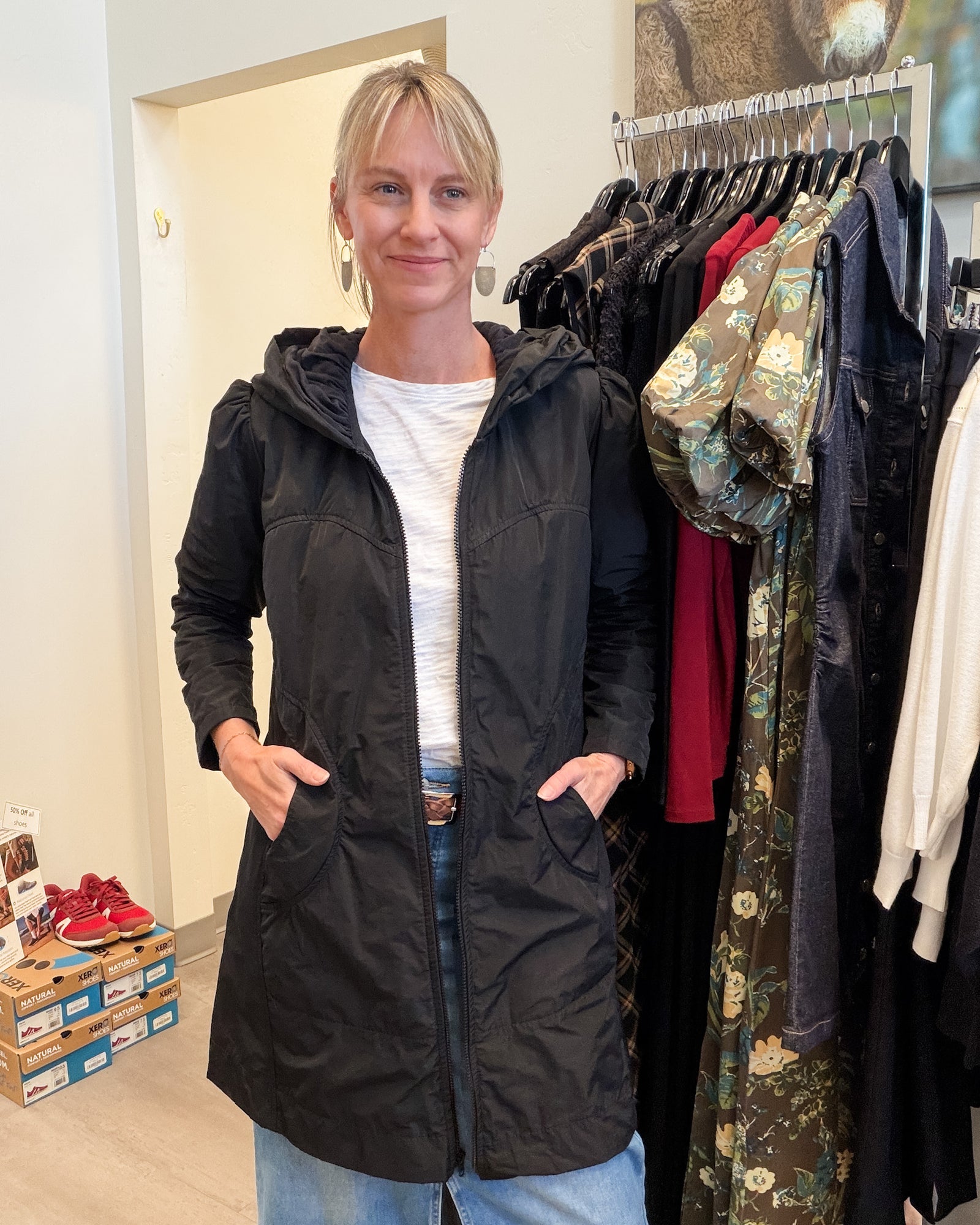 A woman wearing a bright red hooded jacket with a black inner lining, layered over a white top and blue jeans, standing against a plain white wall.