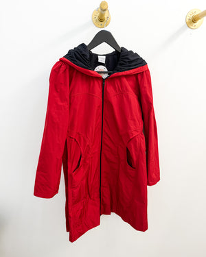 A red hooded zip-up jacket with a black hood lining, hanging on a black hanger against a white wall.
