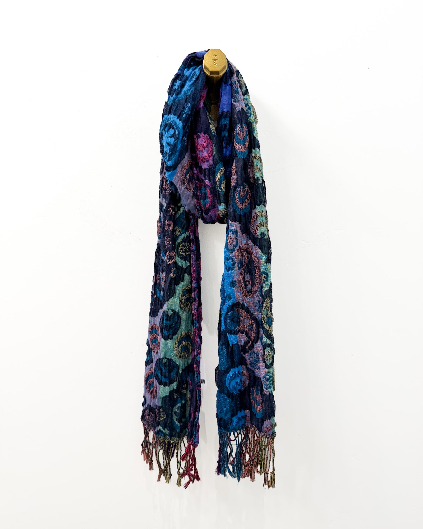 A close-up of a person wearing a dark scarf with a colorful paisley and medallion pattern in blue, purple, teal, pink, and beige, paired with a dark gray blazer.