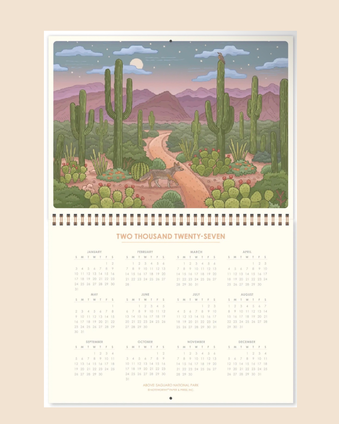 A spiral-bound 2027 National Parks wall calendar displayed against a solid beige background. The cover features a colorful landscape illustration of Mount Raina with green hills, wildflowers, pine trees, a wolf, and a bald eagle.