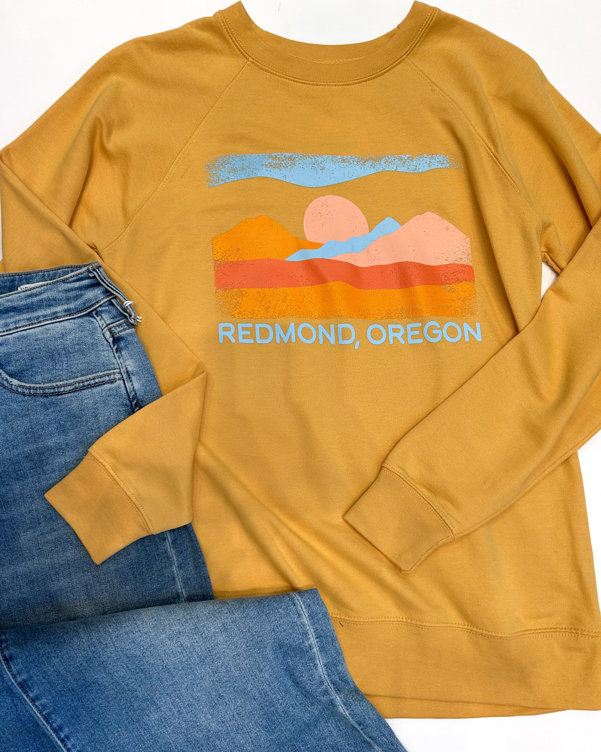 Yellow sweatshirt with a desert landscape graphic and 'Redmond, Oregon' text, paired with blue jeans on a white background.