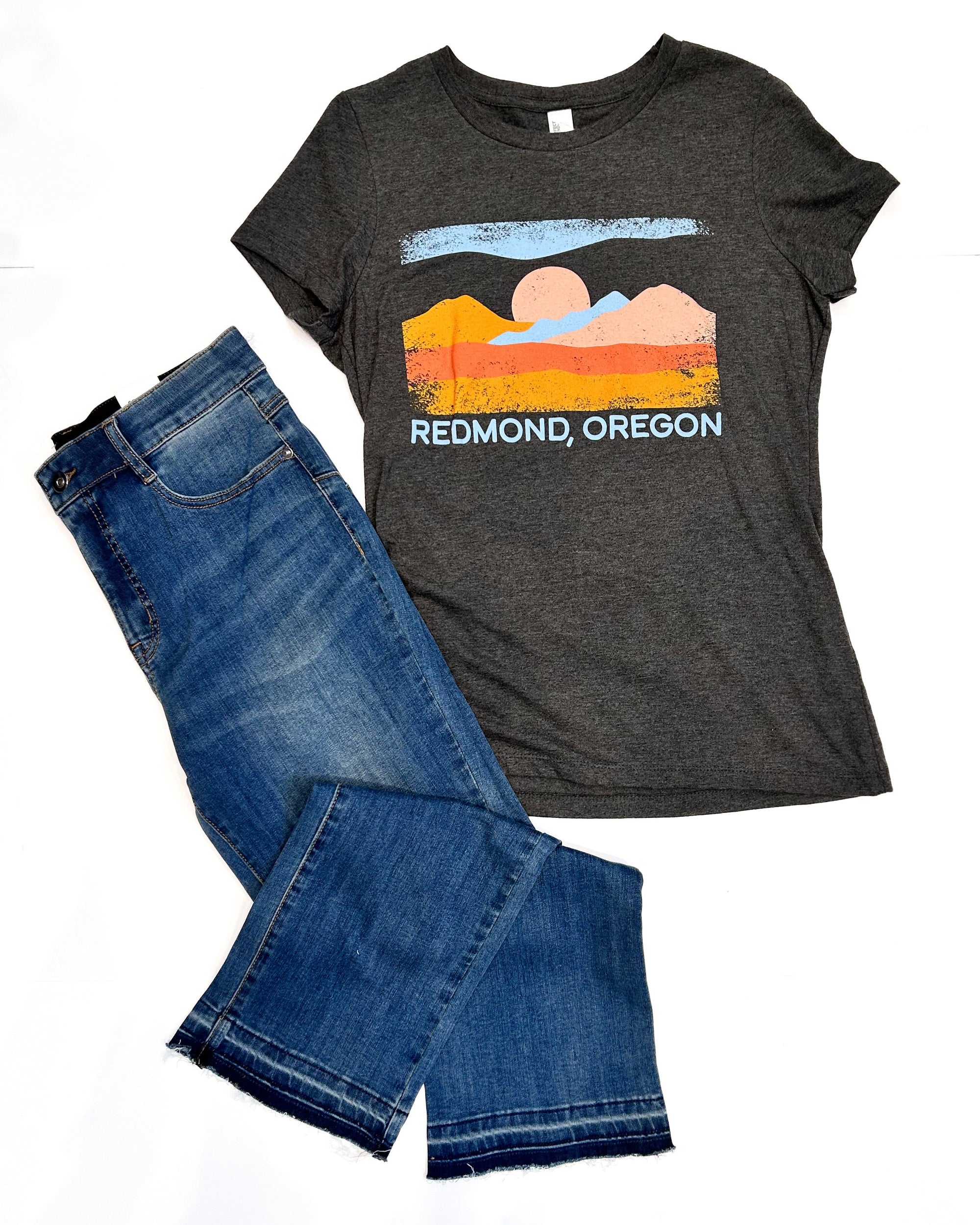 Gray t-shirt with a scenic design and 'Redmond, Oregon' text, paired with blue jeans on a white background.