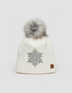 White knit beanie with gray snowflake design and fur pom-pom on a wooden surface