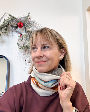 Woman adjusting a colorful scarf in front of a decorative wreath.