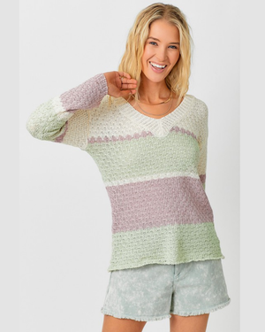 Woman wearing a light green and pink striped sweater with white shorts on a plain background