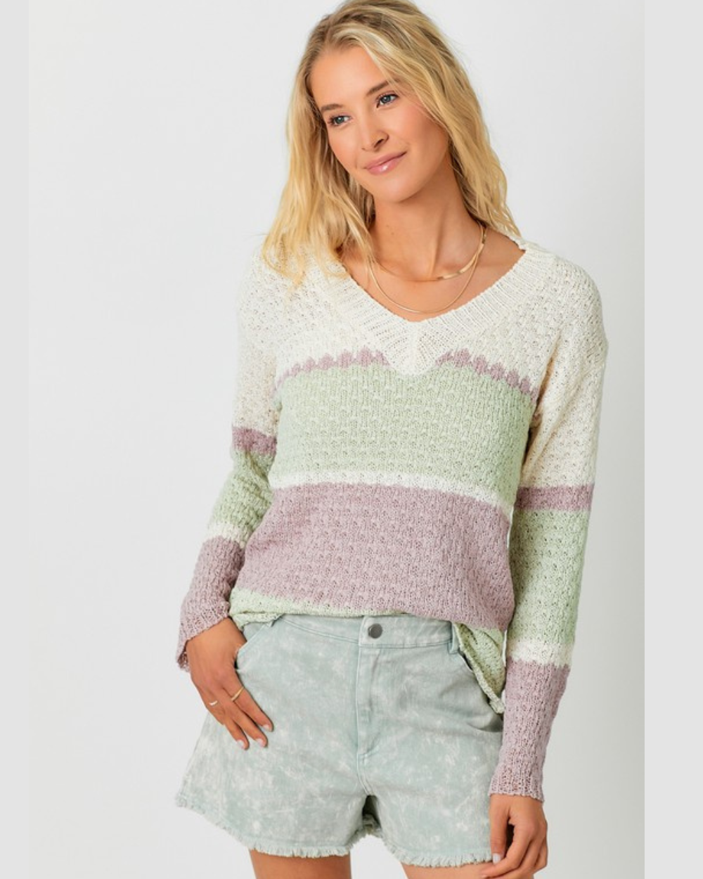 Woman wearing a striped sweater and denim shorts on a plain background