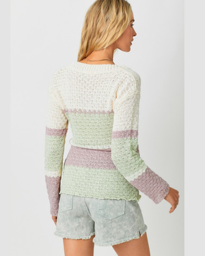 Woman wearing a light green and pink striped sweater with denim shorts on a white background