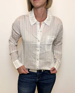 Person wearing a light-colored striped shirt with a collar against a plain background