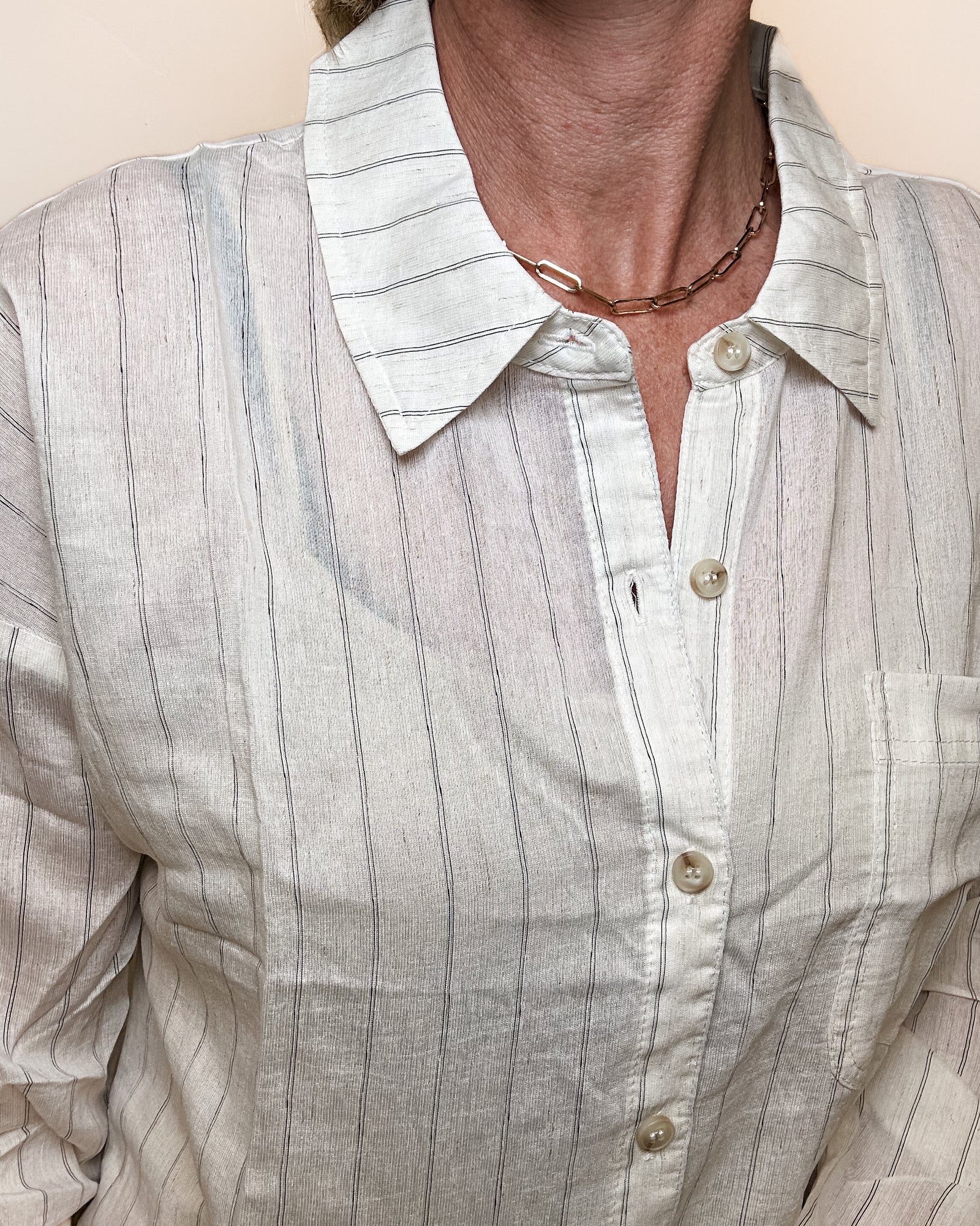 Person wearing a light-colored striped shirt with a collar against a plain background