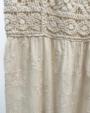 Close-up of a cream-colored dress featuring a textured crochet lace yoke and embroidered floral fabric below.