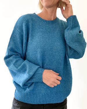 A person wearing a heathered blue knit crewneck sweater with long balloon sleeves and ribbed cuffs, hem, and neckline, shown against a plain white background.