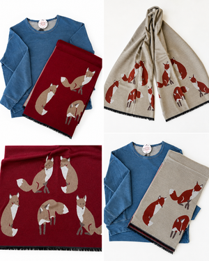 Four product views showing knit scarves with a fox pattern, each paired with a long-sleeve top. The scarves come in blue and beige versions, and the printed fox motifs are in brown, red, and white.