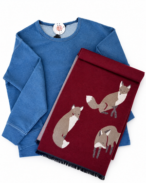 A blue long-sleeve sweatshirt and a folded burgundy throw blanket with fox illustrations, arranged on a white background.