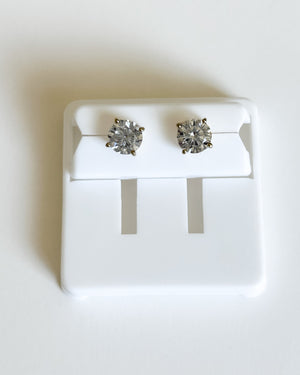 A pair of round-cut stud earrings with silver-toned settings, displayed on a white plastic jewelry stand against a plain white background.