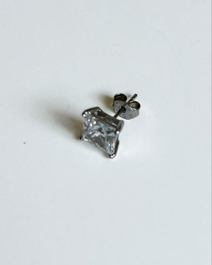 A single silver stud earring with a princess-cut clear gemstone, shown from a side angle with its post and butterfly back visible, on a plain white background.