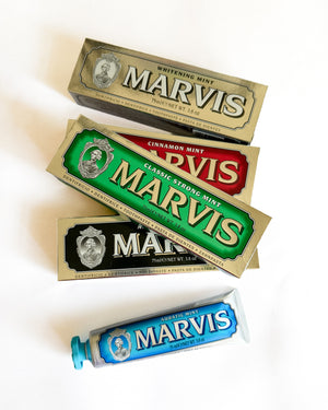 Four Marvis toothpaste boxes and one tube arranged diagonally on a clean white background. The packaging includes Whitening Mint, Classic Strong Mint, and Aquatic Mint flavors in gold, green, red, and blue designs.