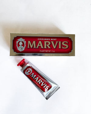 A tube of Marvis Cinnamon Mint toothpaste placed diagonally in front of its original packaging box on a plain white background.