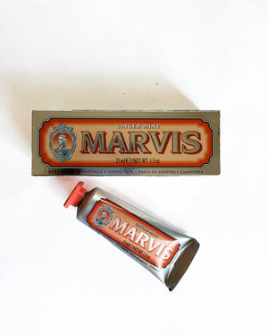 A tube of Marvis Ginger Mint toothpaste with a red cap lies diagonally in front of its original cardboard packaging box on a plain white background.