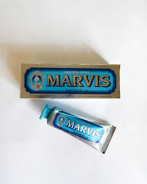 A tube of Marvis Aquatic Mint toothpaste and its original box, both featuring the brand's signature blue and gold packaging, arranged on a plain white surface.