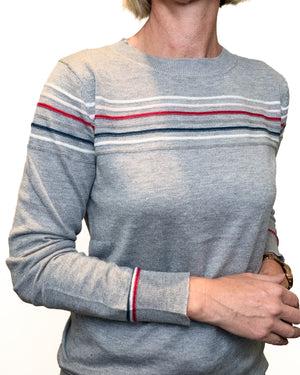 A person wearing a heather gray long-sleeve crewneck sweater with thin horizontal stripes in red, white, and navy across the chest and shoulders, shown against a plain white background.