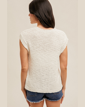 Woman wearing a textured white top and denim shorts on a plain background