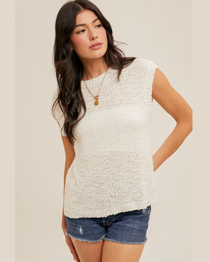 Woman wearing a textured white sleeveless top and denim shorts on a plain background