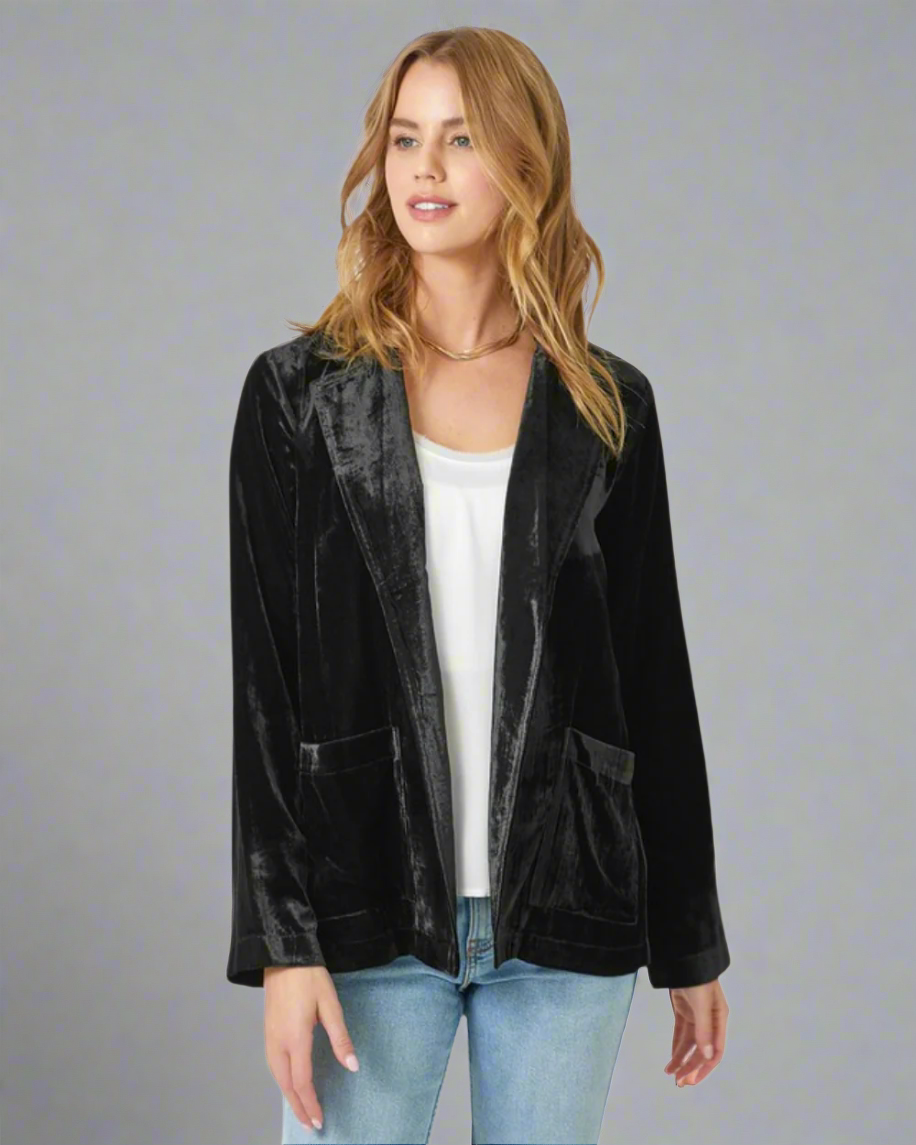 Woman wearing a black velvet jacket over a white top and blue jeans on a white background