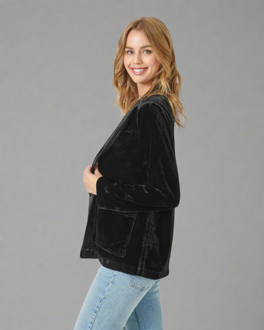 Woman wearing a black velvet jacket over a white top and blue jeans on a white background