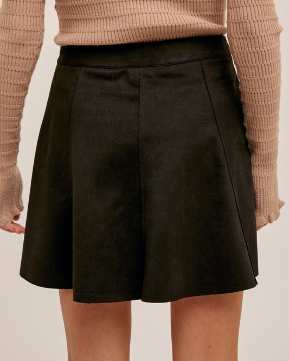 Black skirt worn with a beige sweater on a plain background