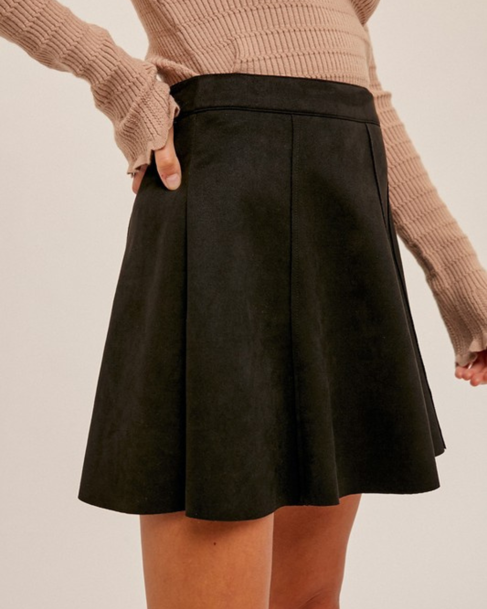 Black skirt worn with a beige sweater on a plain background