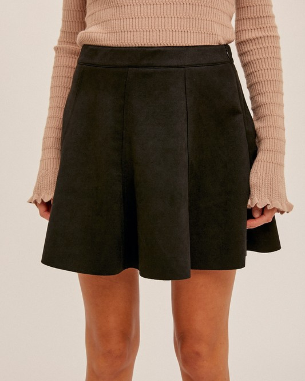 Black skirt worn with a beige sweater on a plain background