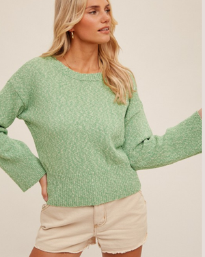 Woman wearing a green sweater and beige shorts against a plain background