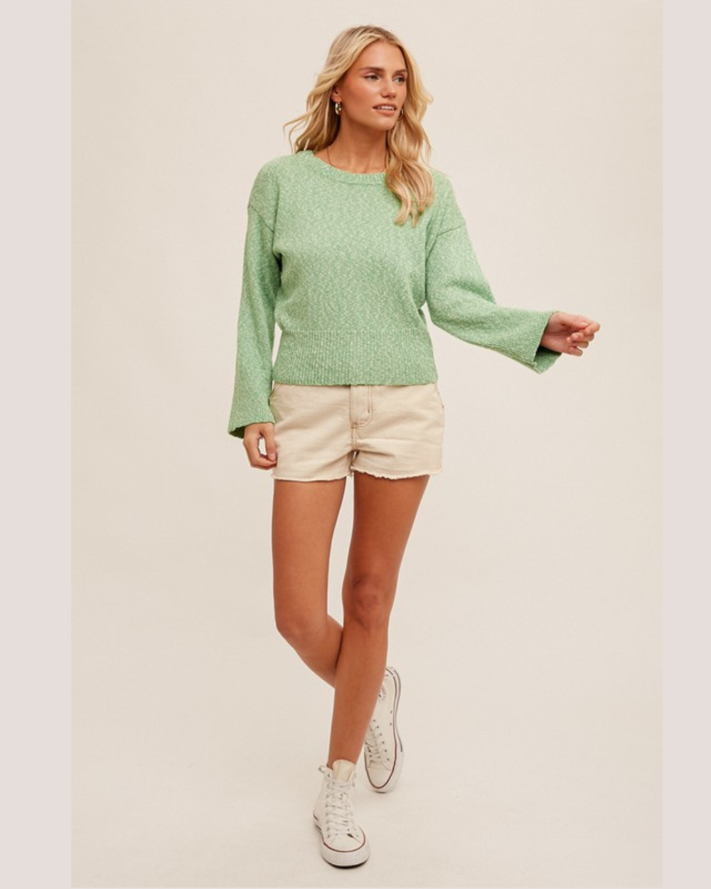 Woman wearing a green sweater and white shorts on a plain background