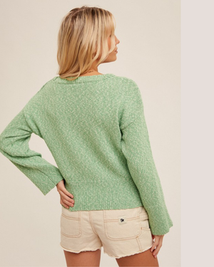 Woman wearing a green sweater and beige shorts against a plain background