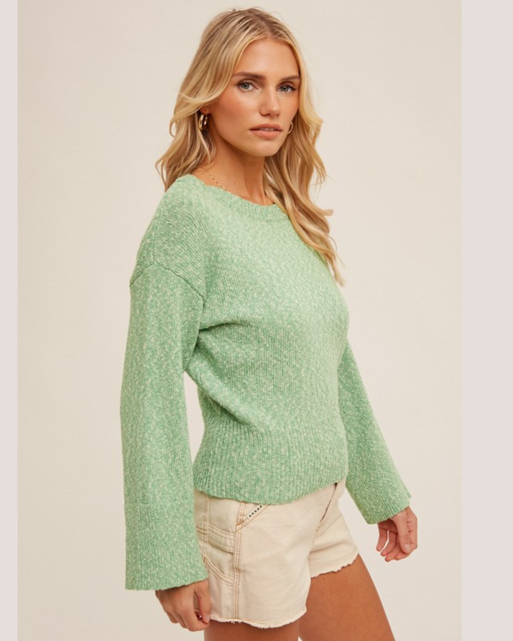 Woman wearing a green sweater and white shorts on a plain background