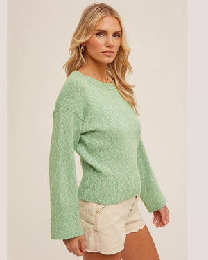 Woman wearing a green sweater and white shorts on a plain background