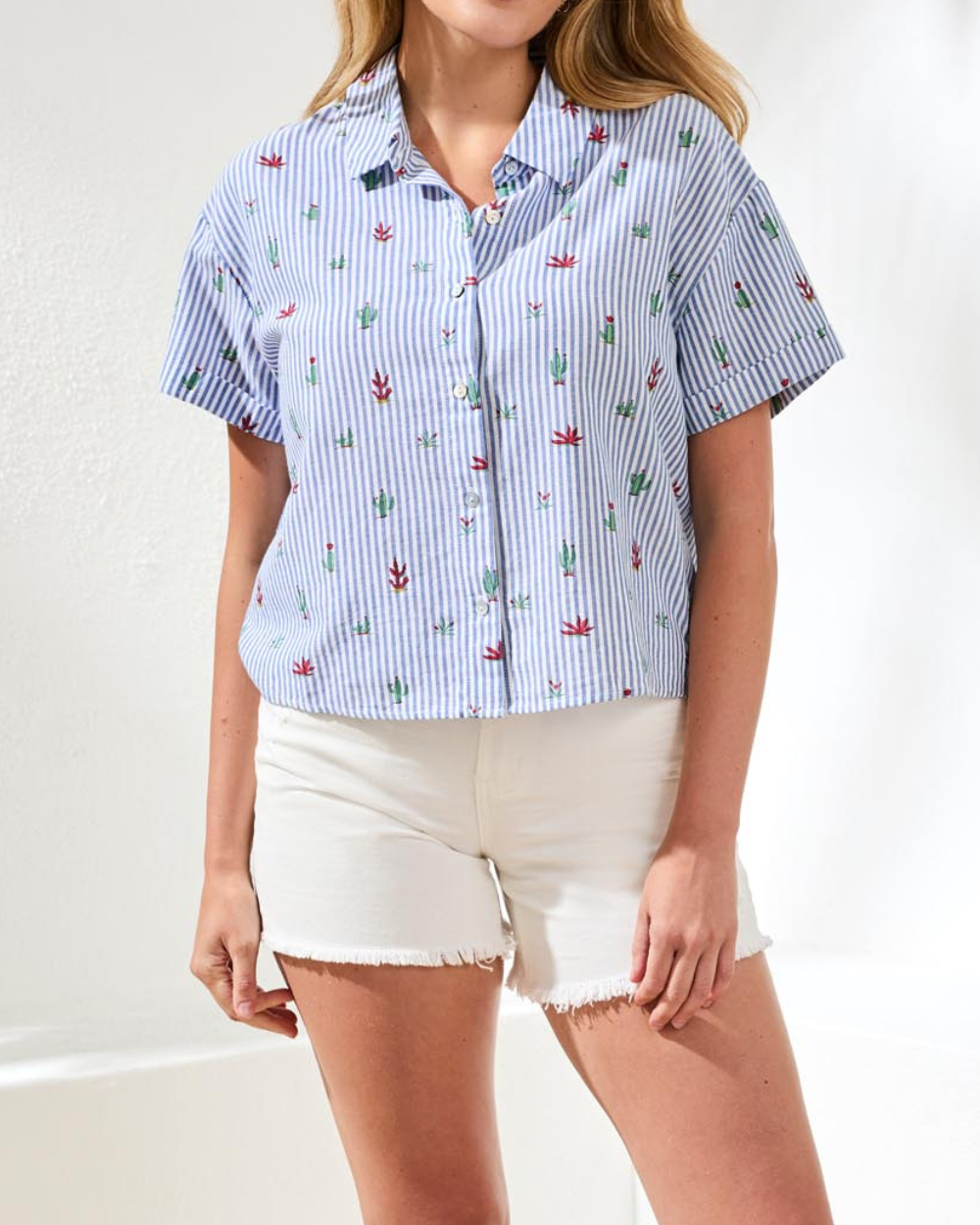 Woman wearing a blue and white striped shirt with floral patterns and white shorts on a white background